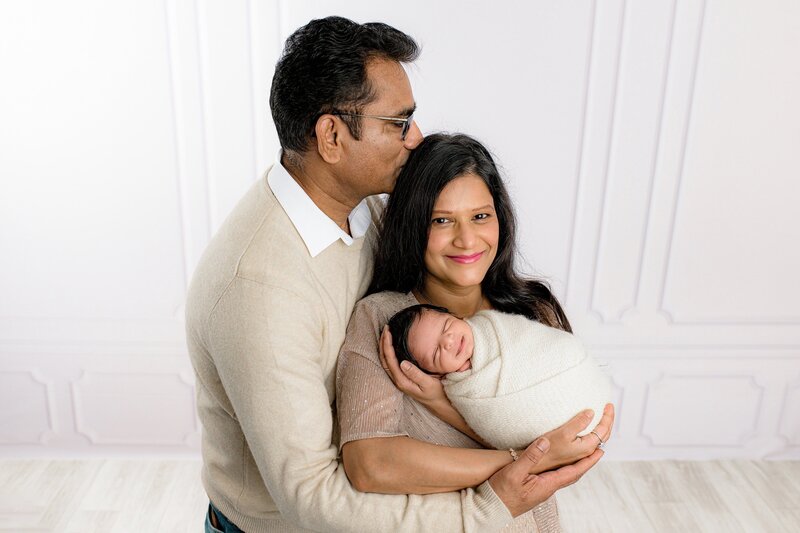 father kisses mother's head as she holds their newborn son