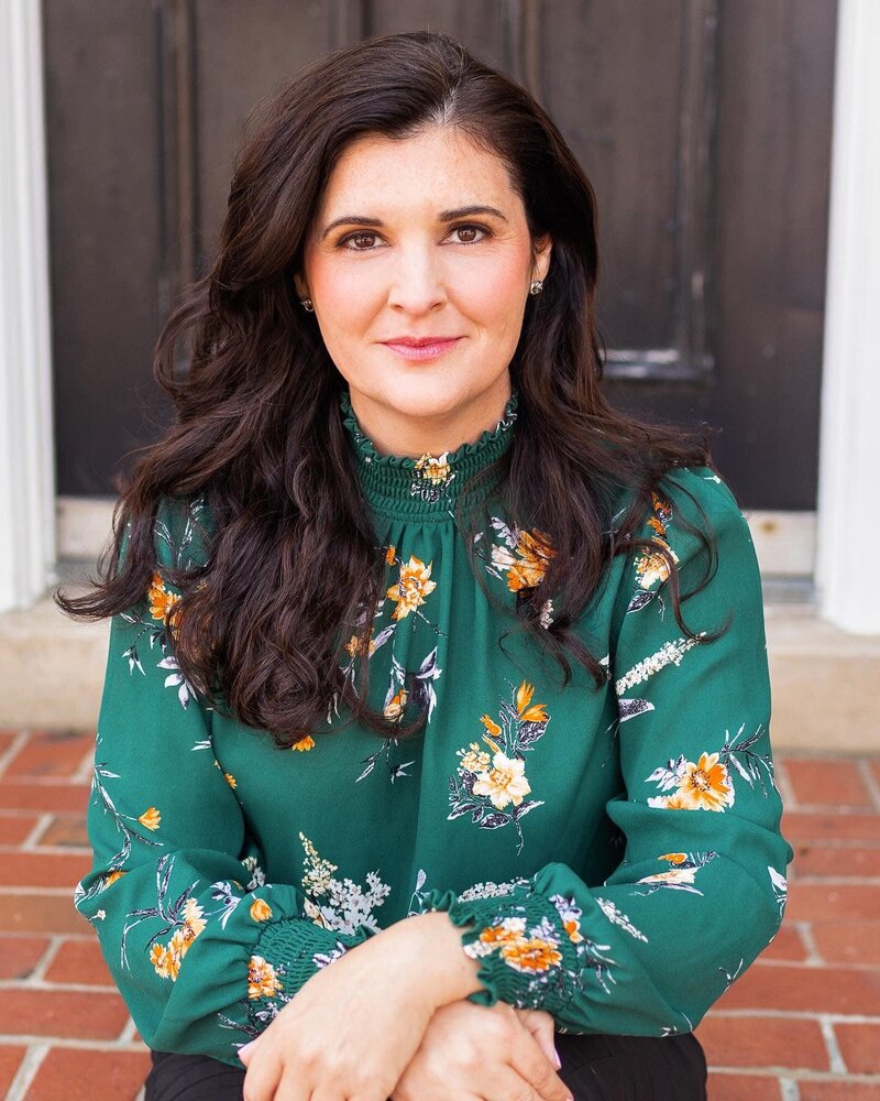 A brunette lady wearing a green floral shirt sitting on brick steps outside