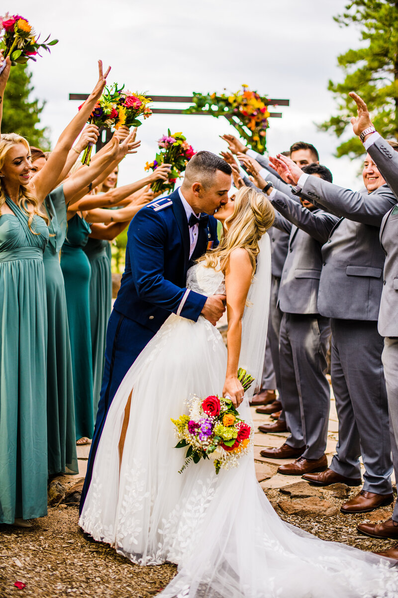 Flagstaff Arboretum wedding couple kissing bridesmaids and groomsmen holding up arms floral arch cheering