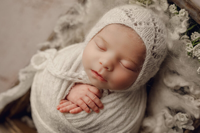 newborn girl wrapped up sleeping wearing all white in a gorgeous studio setting
