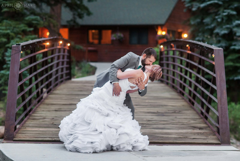 Groom dips his bride in front of Estes Park Condos Bridge on Fall River