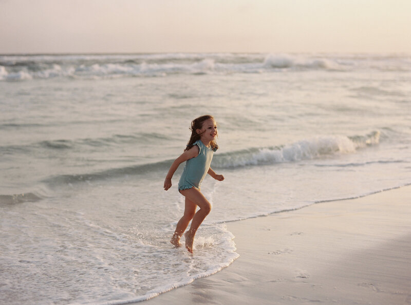 A little girl in a blue swimsuit playing in the waves at the beach in Watercolor, Florida.