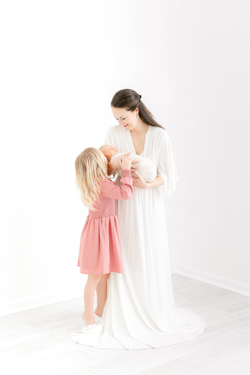 A beautiful family photo in our studio of a mother and her daughter kissing her newborn baby sister by Washington DC Family PhotographerWashington DC Family Photographer