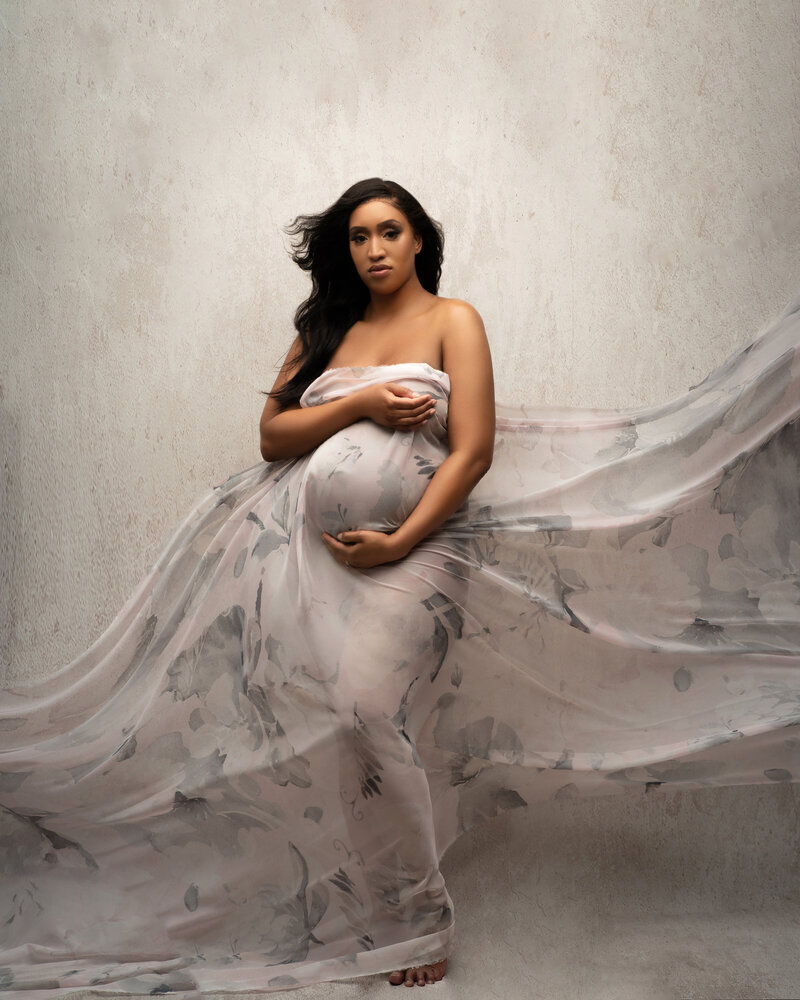 Pregnant woman engulfed in floral flowing fabric while holding pregnant belly