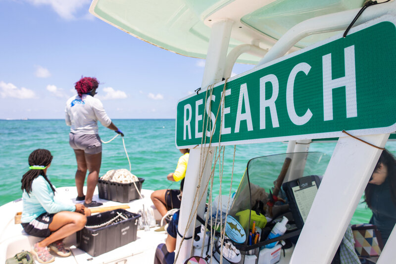 Research Sign in foreground as female shark scientists prepare equipment at the bow of the vessel