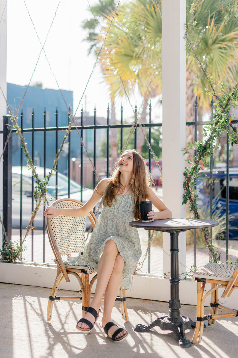 An excited girl celebrates her sixteenth birthday while drinking coffee at a table on a coffee house patio in Galveston