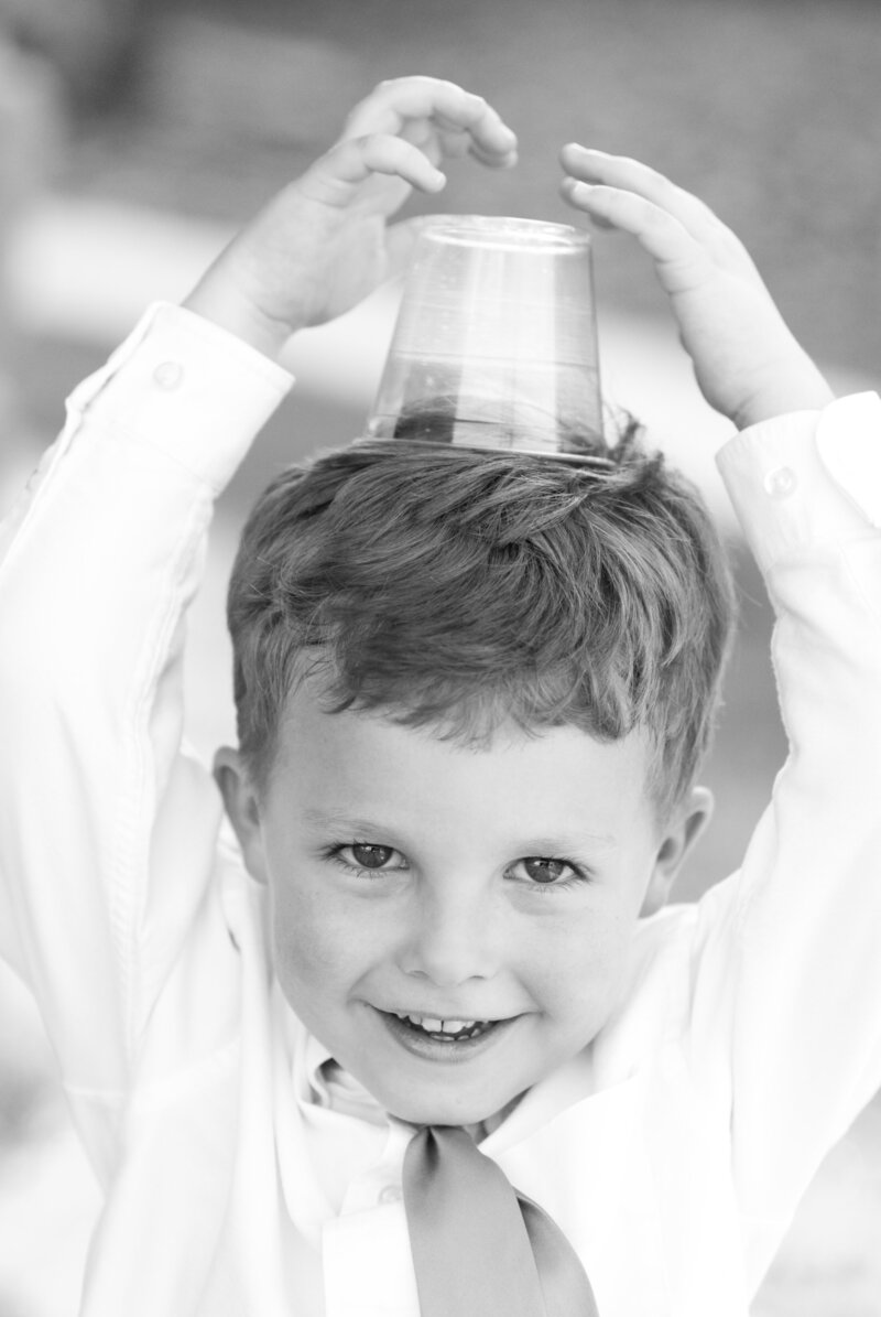 black and white photo of preschool boy holding cup on head