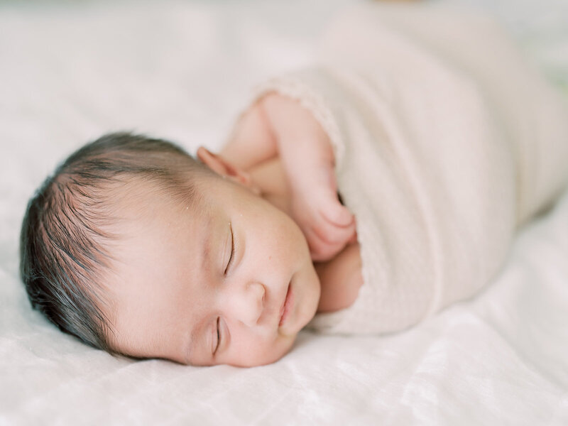 Baby girl swaddles in tan sleeps peacefully on a bed during her Maryland Newborn session.