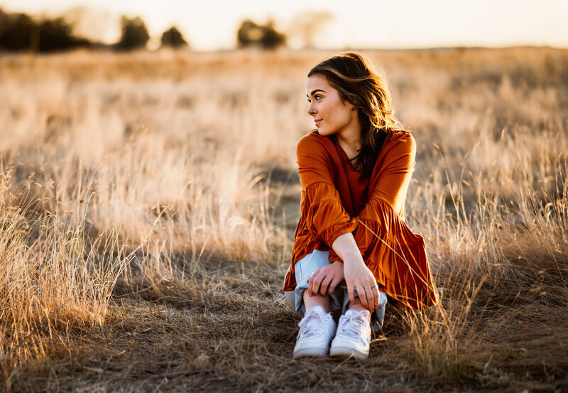 Senior girl sits in field of grass looking off into the distance