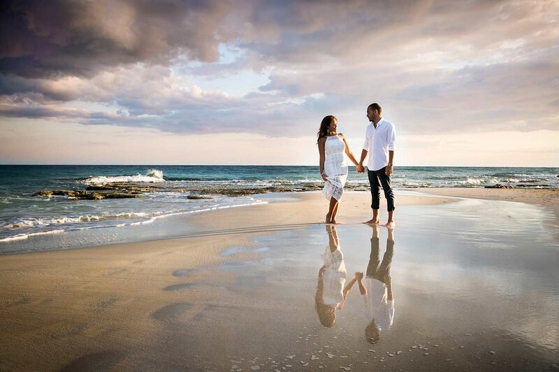 Bride & groom standing on the sand surrounded by water at sunset