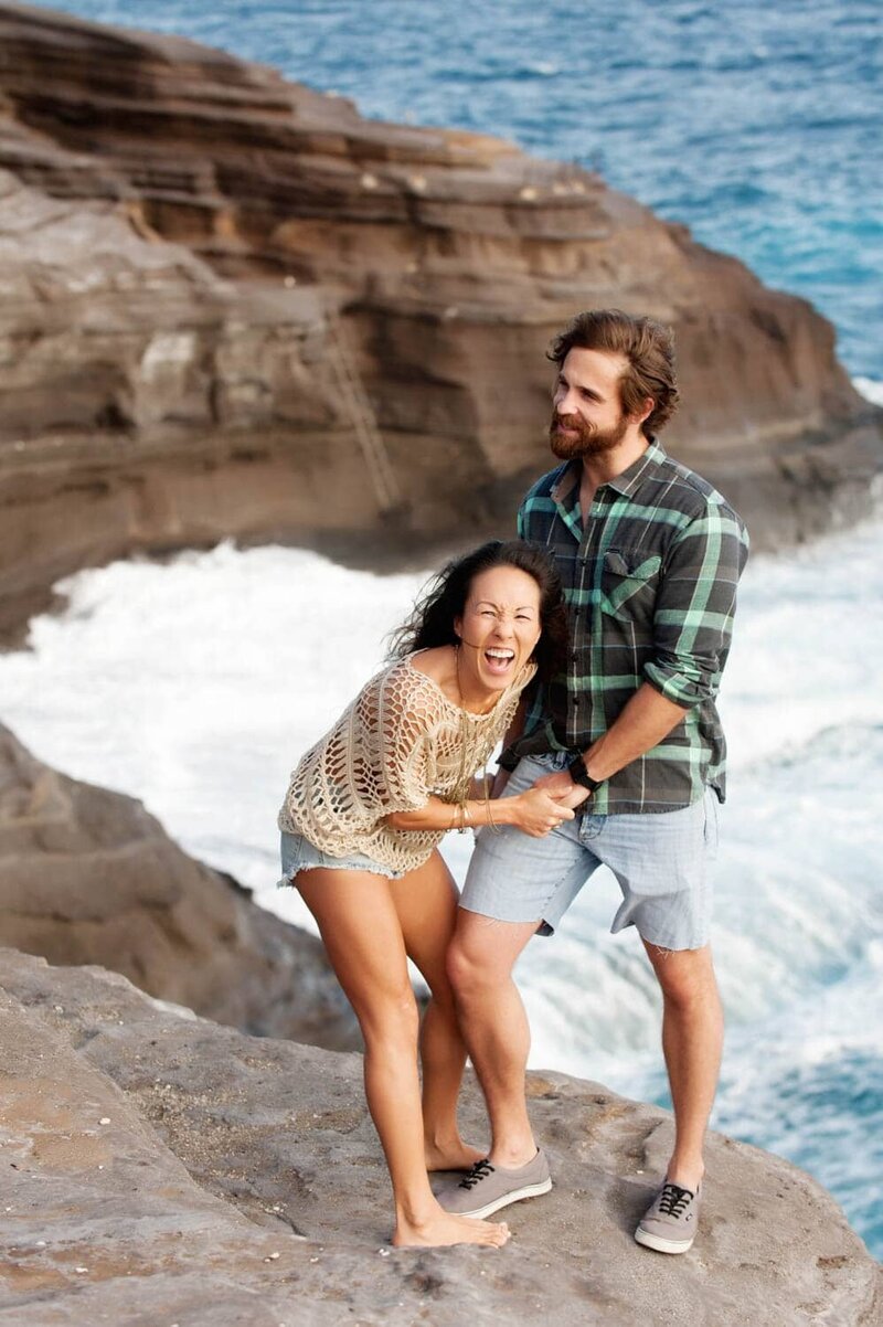 a woman laughs while holding a man's hands at spitting caves in hawaii