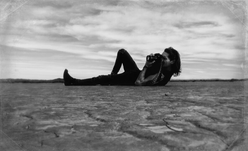 Behind the scenes Photographer Mark Maryanovich lying on desert sand looking through camera back
