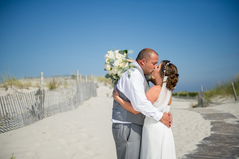 bride and groom kiss on beach walkway