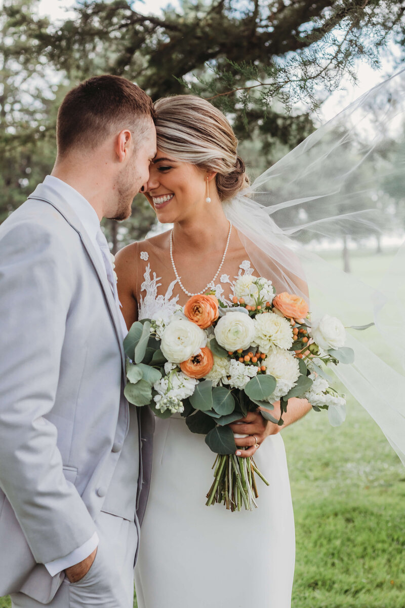 Wedding couple holding bouquet with veil blowing in wind
