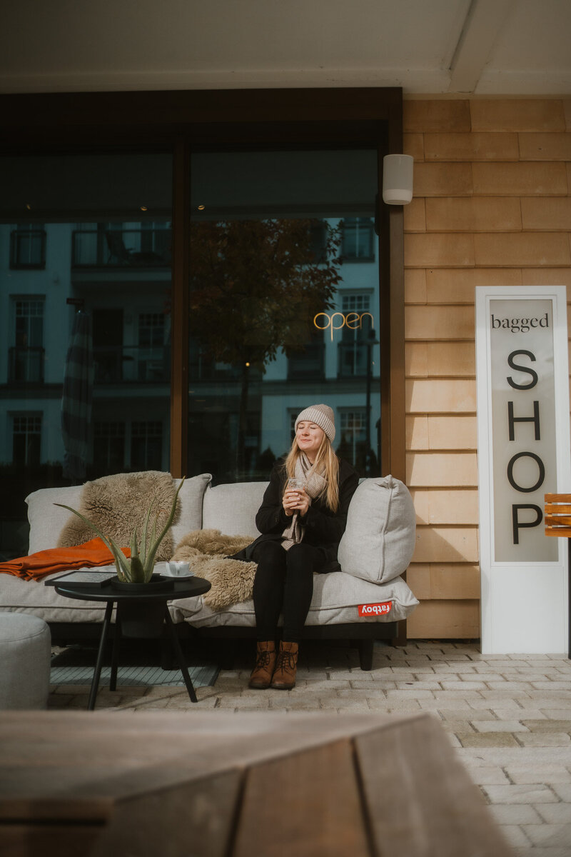 Frau mit Kaffee sitzend auf der Außenterrasse vor dem Shop bagged im Hotel the breeze.