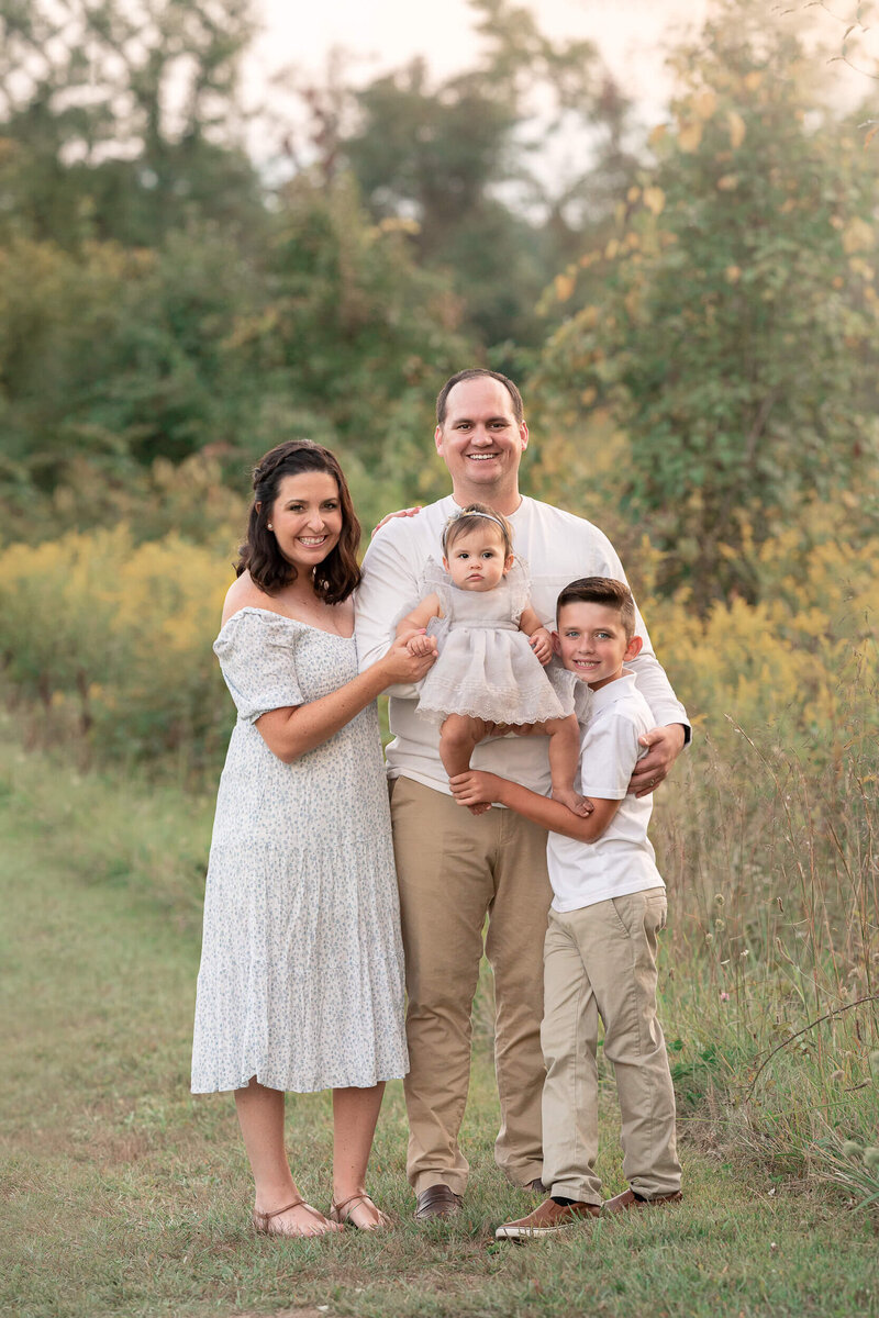 family of four smiles outside in field