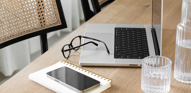 Laptop sitting on a table with glasses of water, notebook, cell phone, and glasses