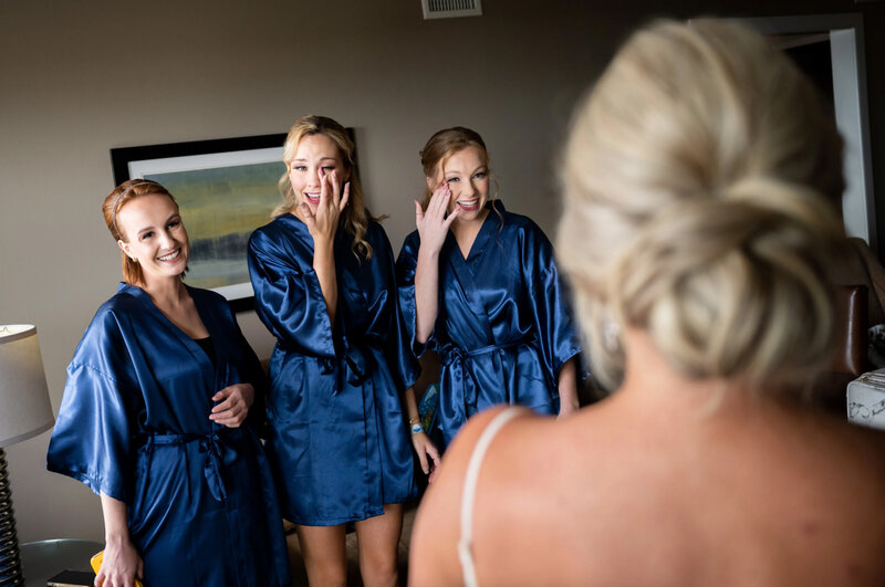 Bridesmaids wearing blue satin robes, crying after seeing their friend for the first time in her wedding gown before her wedding at the Icona Windrift hotel in Avalon, New Jersey