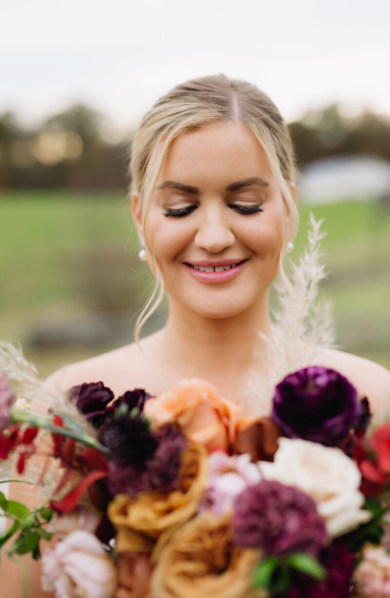bride holding her purple and orange floral bouquet up to her face and smiling as she looks down at it photographed by charlottesville wedding photographers