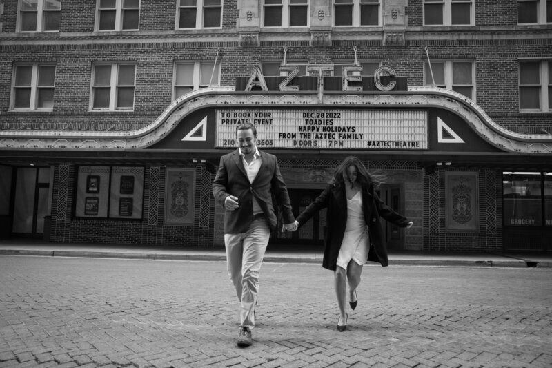 A black and white photo of a couple walking in front of a theater, captured by an Austin wedding photographer.