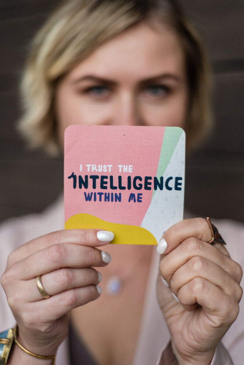 Lady holding a pink card that reads I trust the intelligence within me - Ania Volovique empowerment and mindset coach
