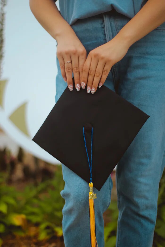 A college senior holding her graduation cap. Showing the daunting life transition that comes with graduating college. With the support of a group therapist that transition can be easier. Get peer support through therapy in Manhattan.