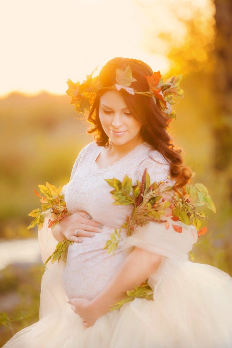 Fall themed pregnancy photo by the Laramie river with a mom wearing a long ivory dress and a floral garland.