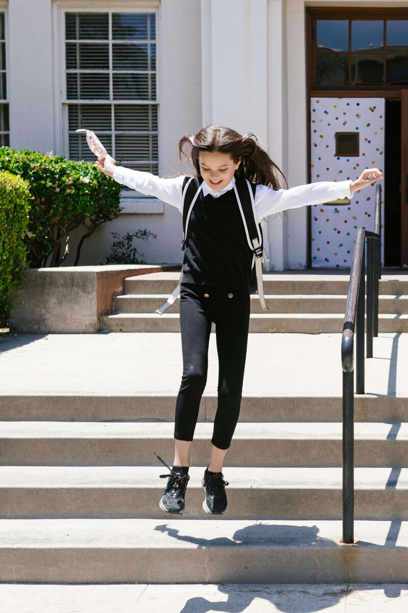 A happy middle school female student jumping off steps with her hands in the air