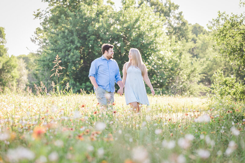 Man and woman holding hands walking in field of wildflowers, Austin Family Photographer