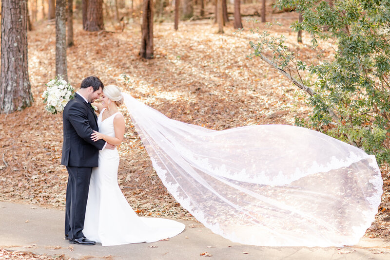 bride and groom embracing in the woods while bride's veil hangs in the wind