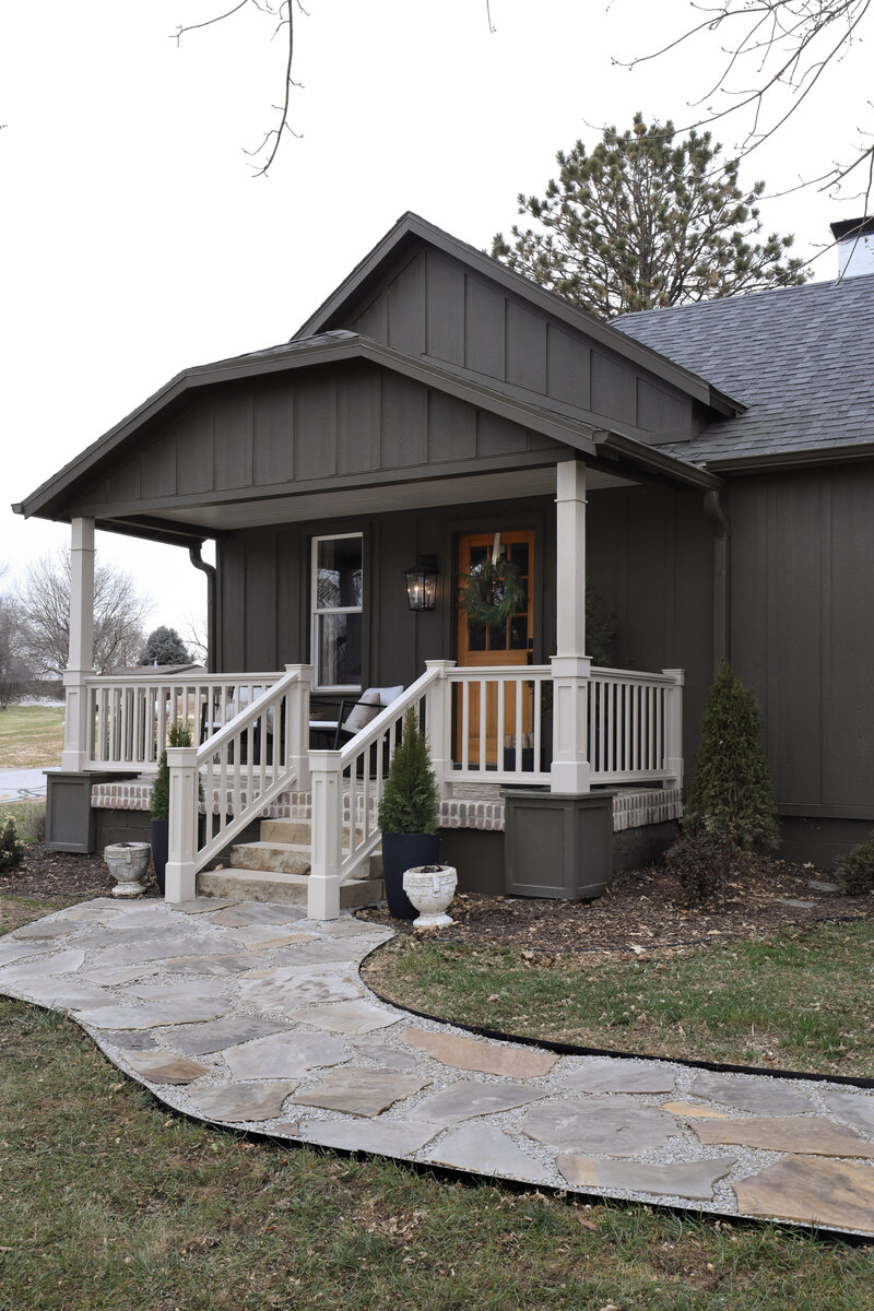 The exterior project by Nadine Stay. Board and batten siding install. Muddled Basil by Sherwin Williams exterior paint color. Flagstone path, brick front porch floor, and a custom built railing. Cabin exterior.