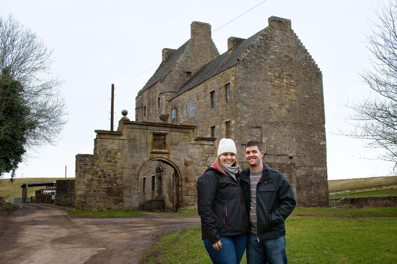 Melissa Driggers posing with her husband in front of Midhope Castle Scotland.