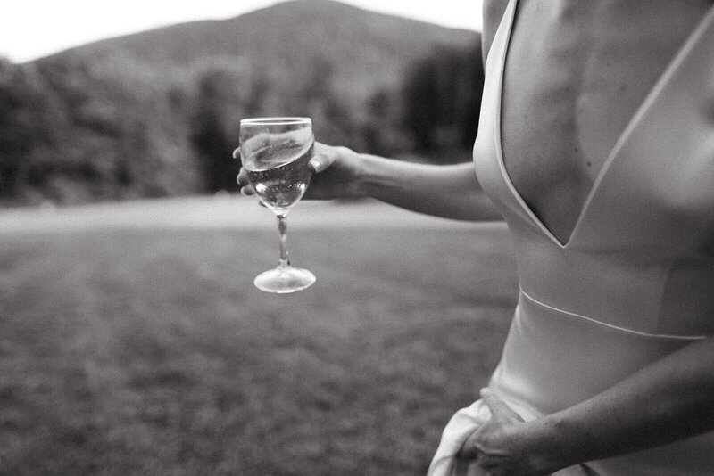 A bride in the mountains holding a glass of white wine