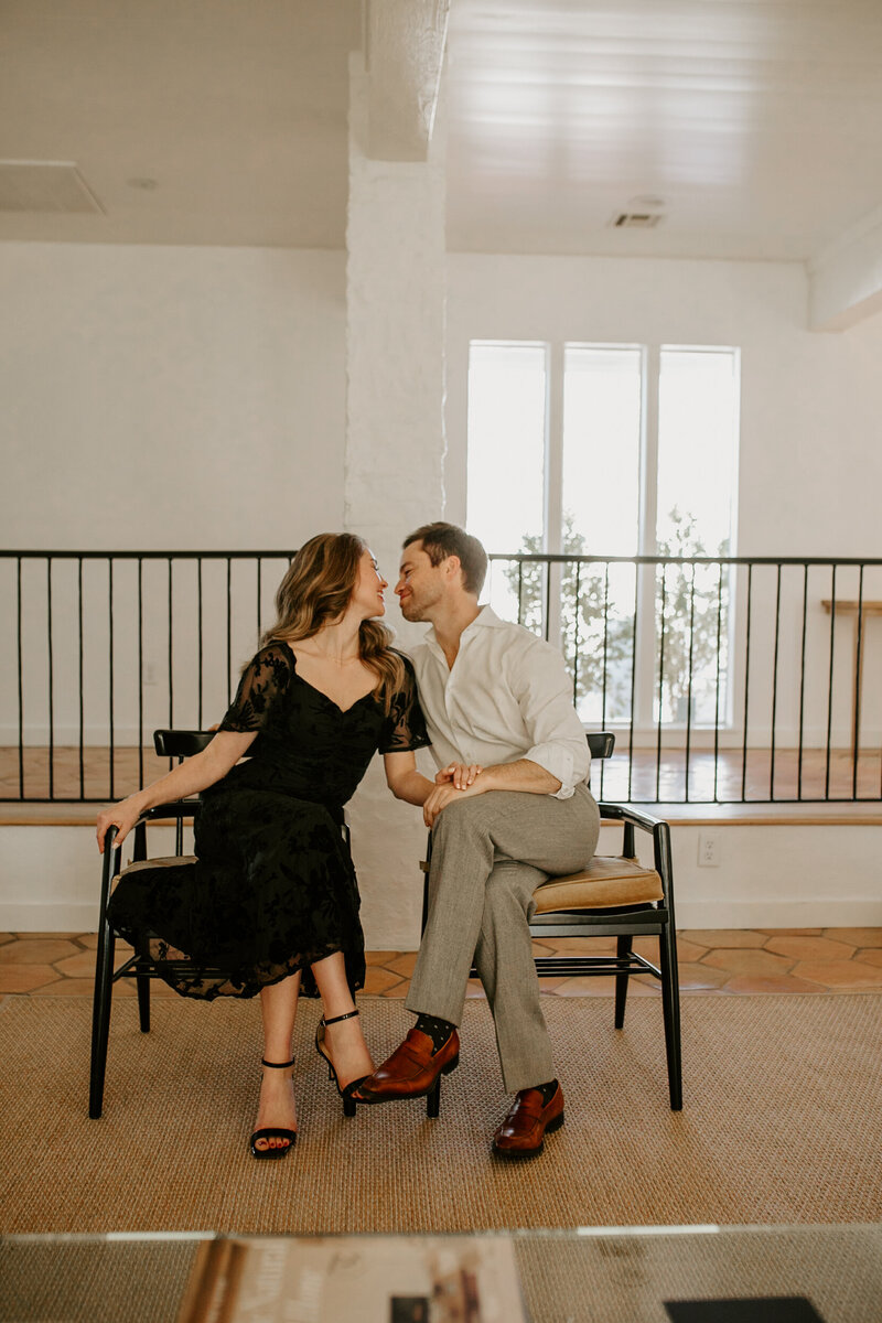Couple in dress attire sitting together leaning in for a kiss