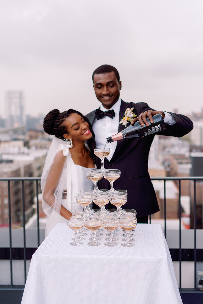 Wedding couple pours champagne tower on wedding day in black tie outfits