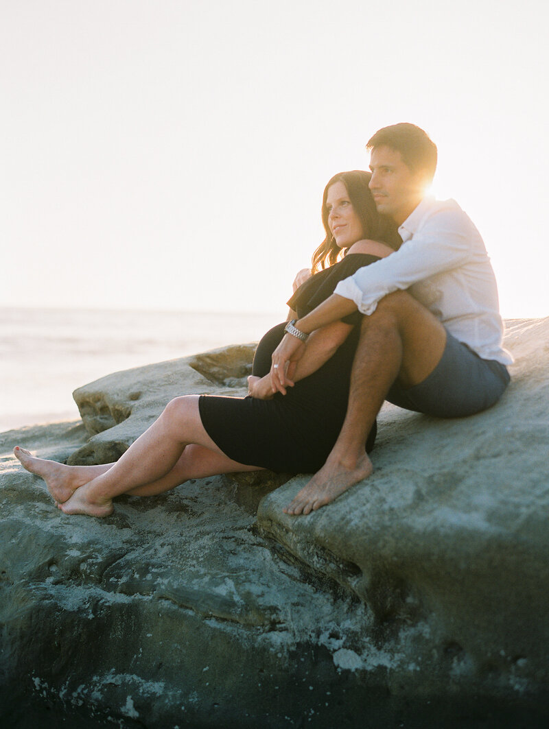 photo of couple sitting on rock during maternity session at wind n sea beach in la jolla, ca