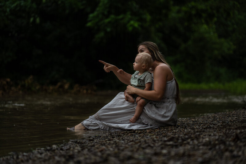 mom and baby posing in a creek pointing at the rocks