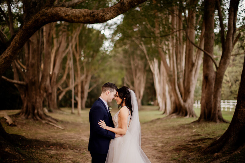 Wedding couple leaning their heads towards each other in the middle o the woods