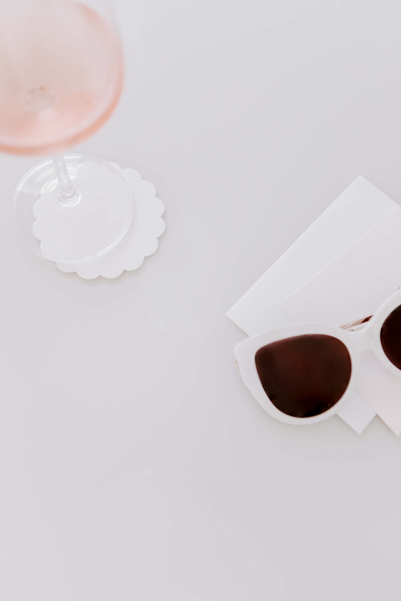 white sunglasses on a table with rose in a wine glass