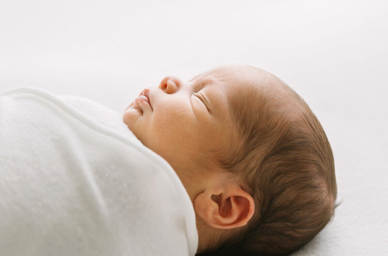 A side profile of a newborn baby wrapped in a whitel swaddle