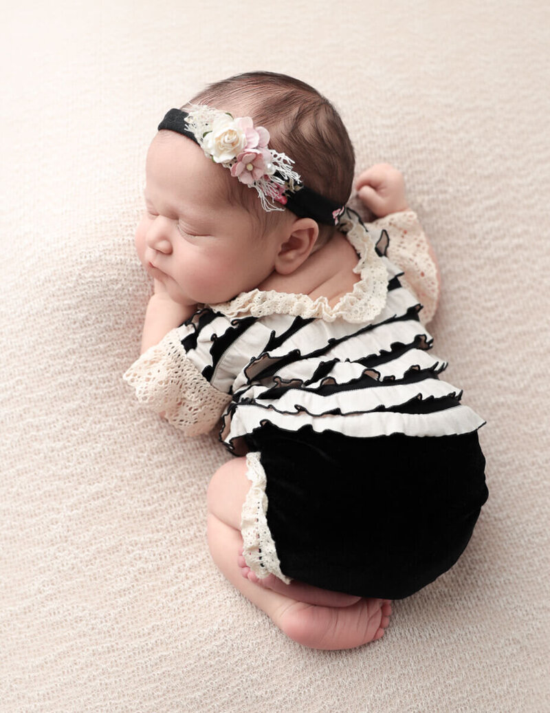 Arial view of a peaceful sleeping newborn girl dressed in a black and tan outfit, captured during a studio session for newborn photography in Rochester, NY.
