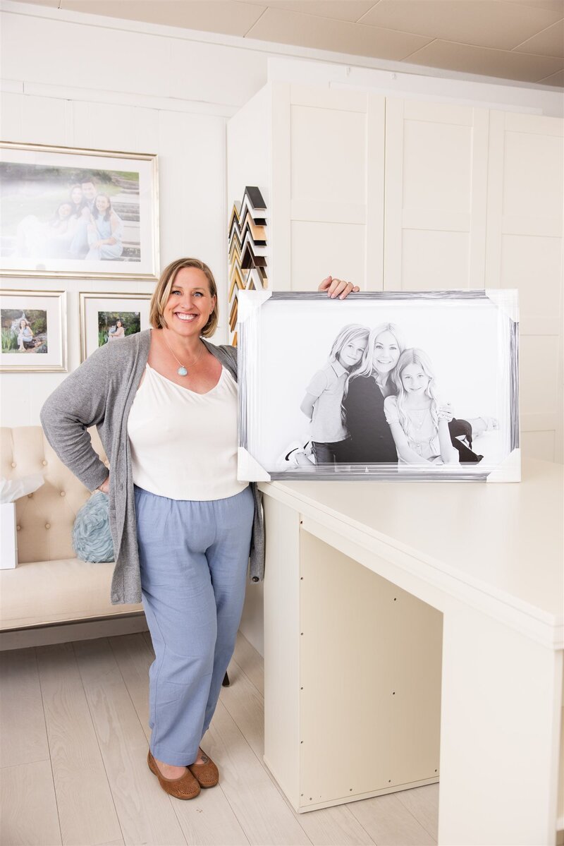Best Boies, Idaho Photographer Tiffany Hix standing in her Boise photography studio holding a framed family portrait.