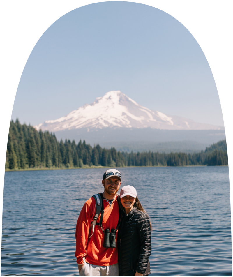 Jenna and Miles standing and smiling at the camera in front of a lake and mountain