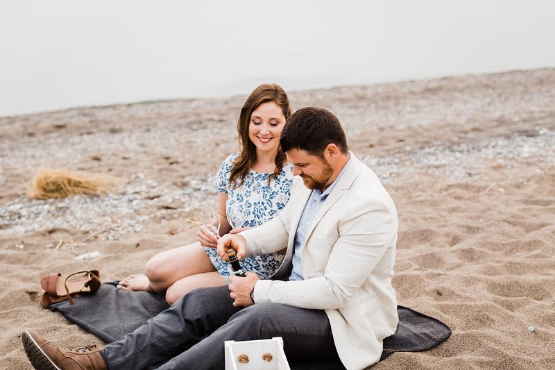 Guy opens a bottle of champagne at point pelee beach during their summer engagement session