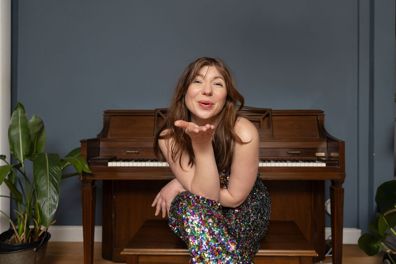A woman blowing a kiss while sitting at a wooden piano