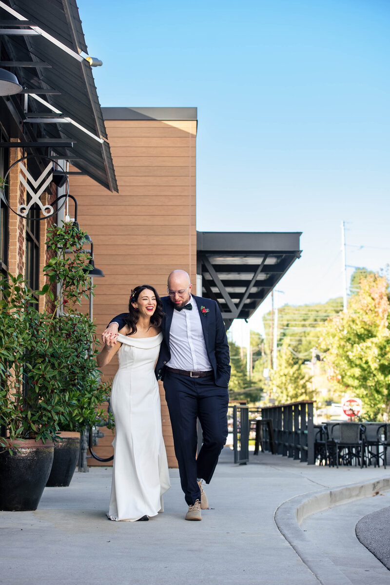 Bride-and-groom-laughing-and-walking-toward-camera-outside-Eventide-Brewing-in-Atlanta