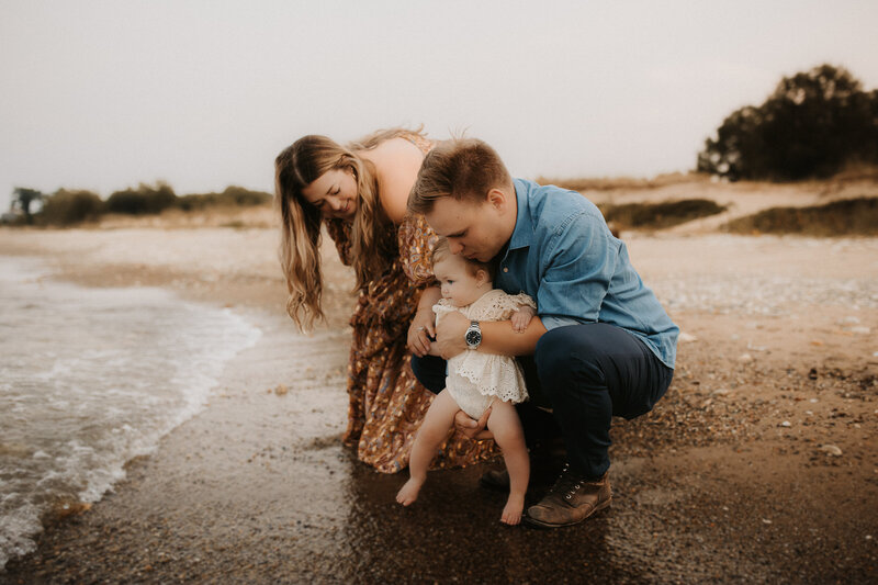 Mom and dad holding their toddler at a Kenosha lake beach.