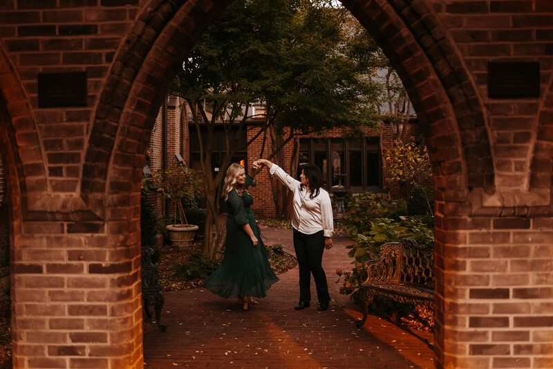 lesbian couple twirling and dancing under brick arch