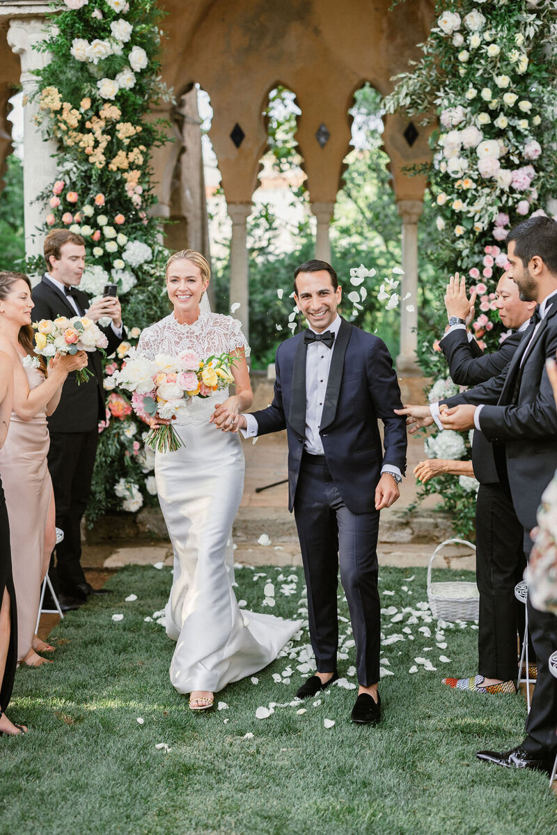 Wedding reception tables set up in an outdoor arched corridor overgrown with ivy