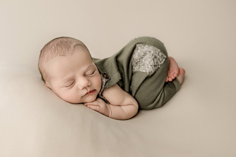 Studio newborn session of baby boy curled up with his bum in the air wearing overalls and his hand placed gently under his cheek